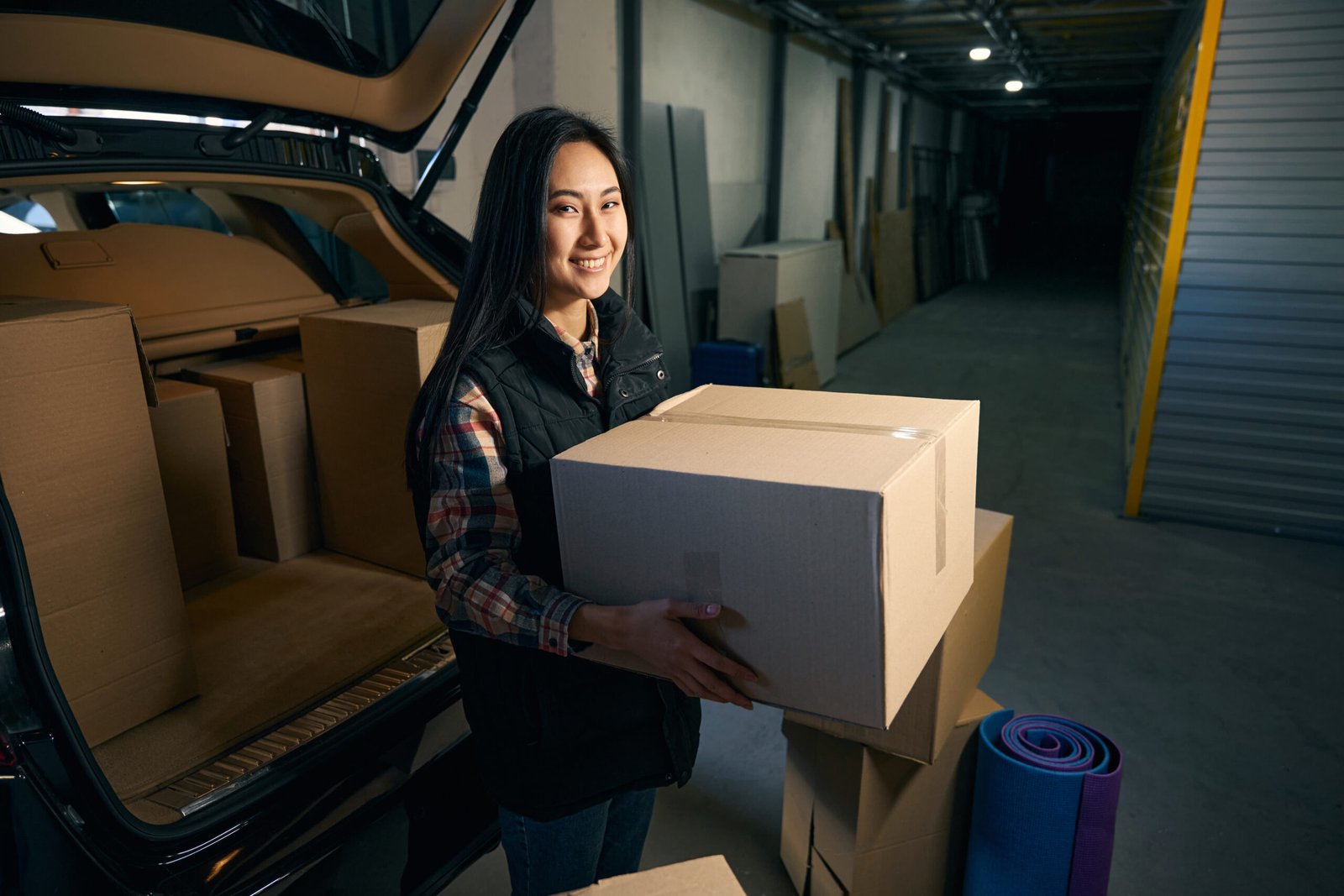 Beautiful female holding a box in her hands while sitting in a car in the trunk of a storage service